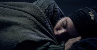 pessoa em situação de rua dormindo enrolado a cobertor