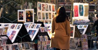 mulher passa por uma calçada com vários quadros expostos